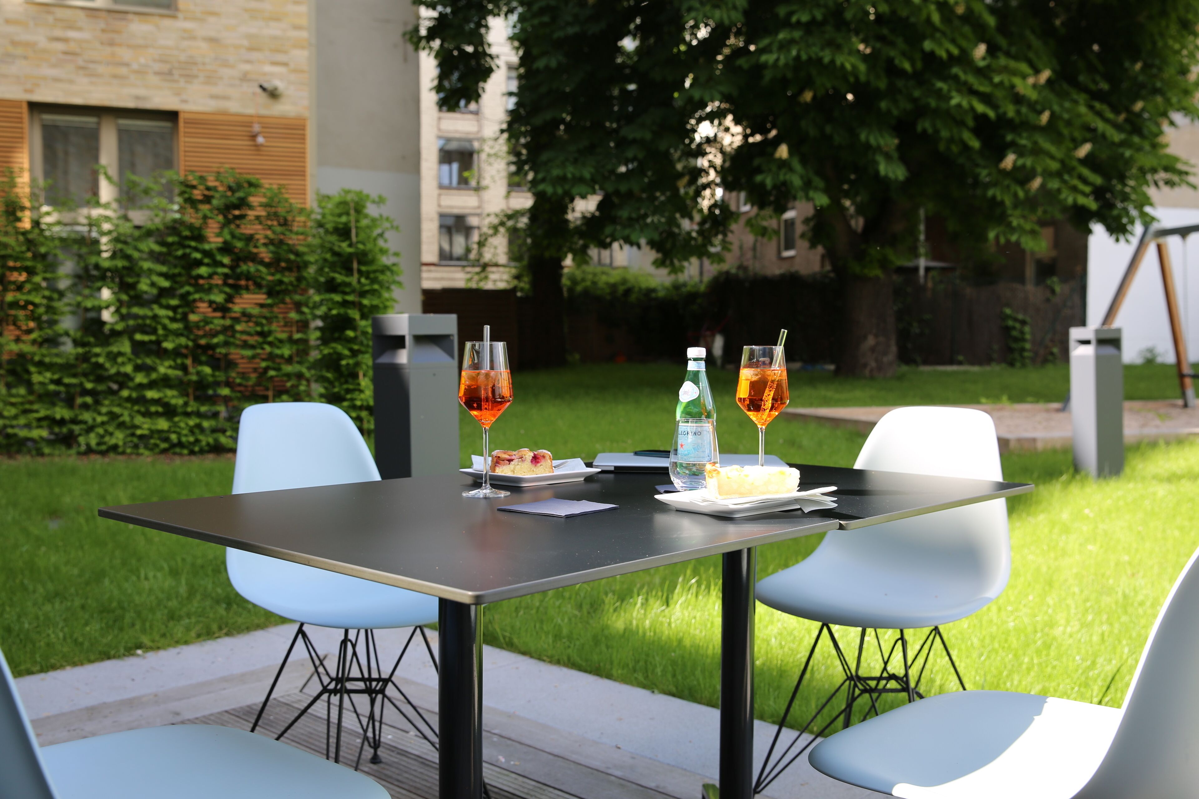 An outdoor dining area with a table and chairs, a bottle of water, glasses, and a slice of cake.