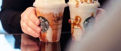 Two Starbucks iced drinks with whipped cream and caramel drizzle, held by a person.