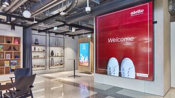 A modern hotel lobby with a large red welcome sign, a reception desk, and a display of shoes.