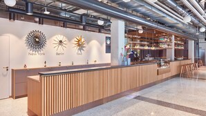 Ein Empfangsbereich mit einem Holzbüro, einer Bar mit Regalen voller Flaschen und Wanddekorationen, die New York, Berlin und Tokio darstellen.