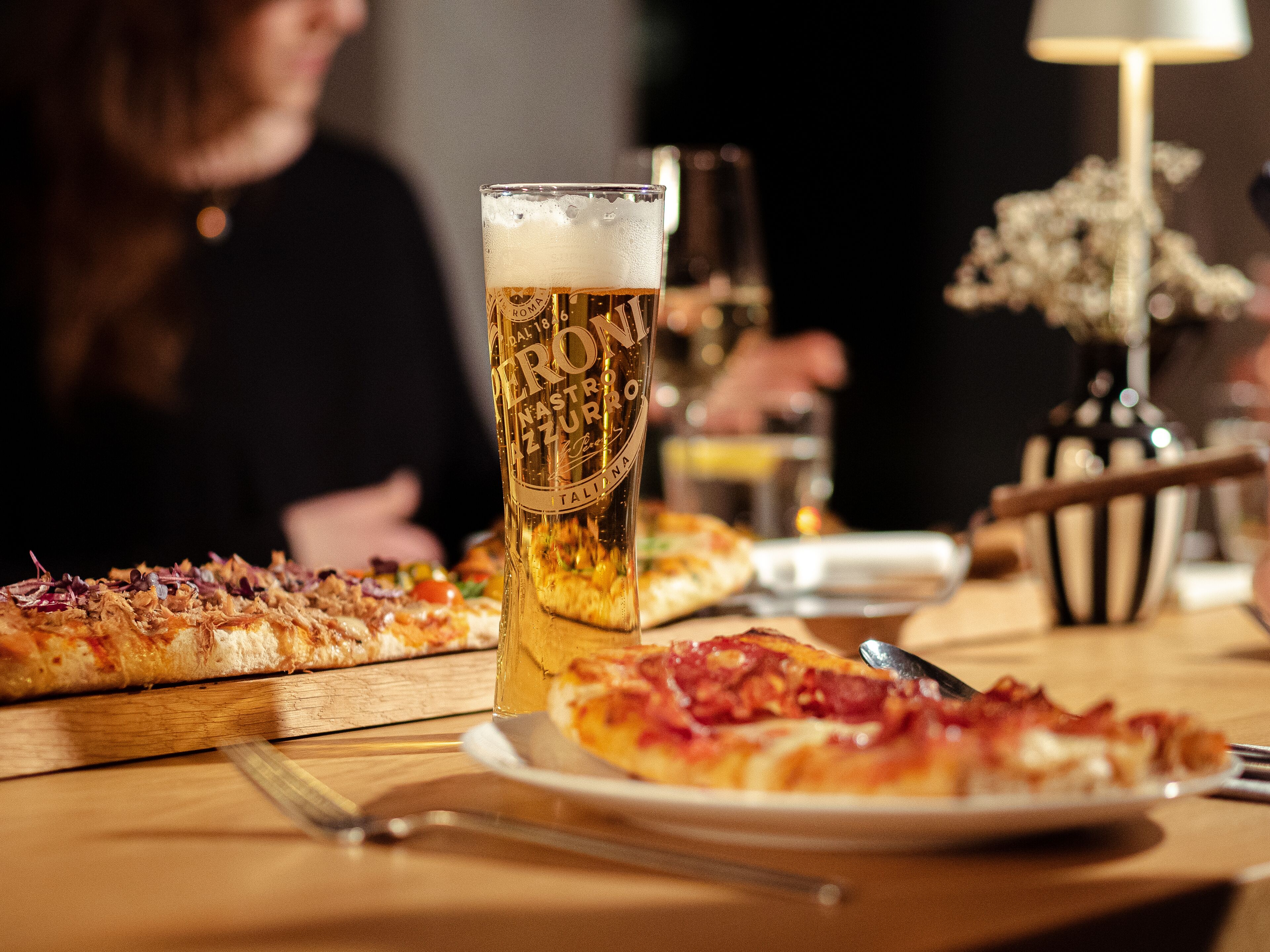 Una mesa con un vaso de cerveza, una pizza y un tenedor.