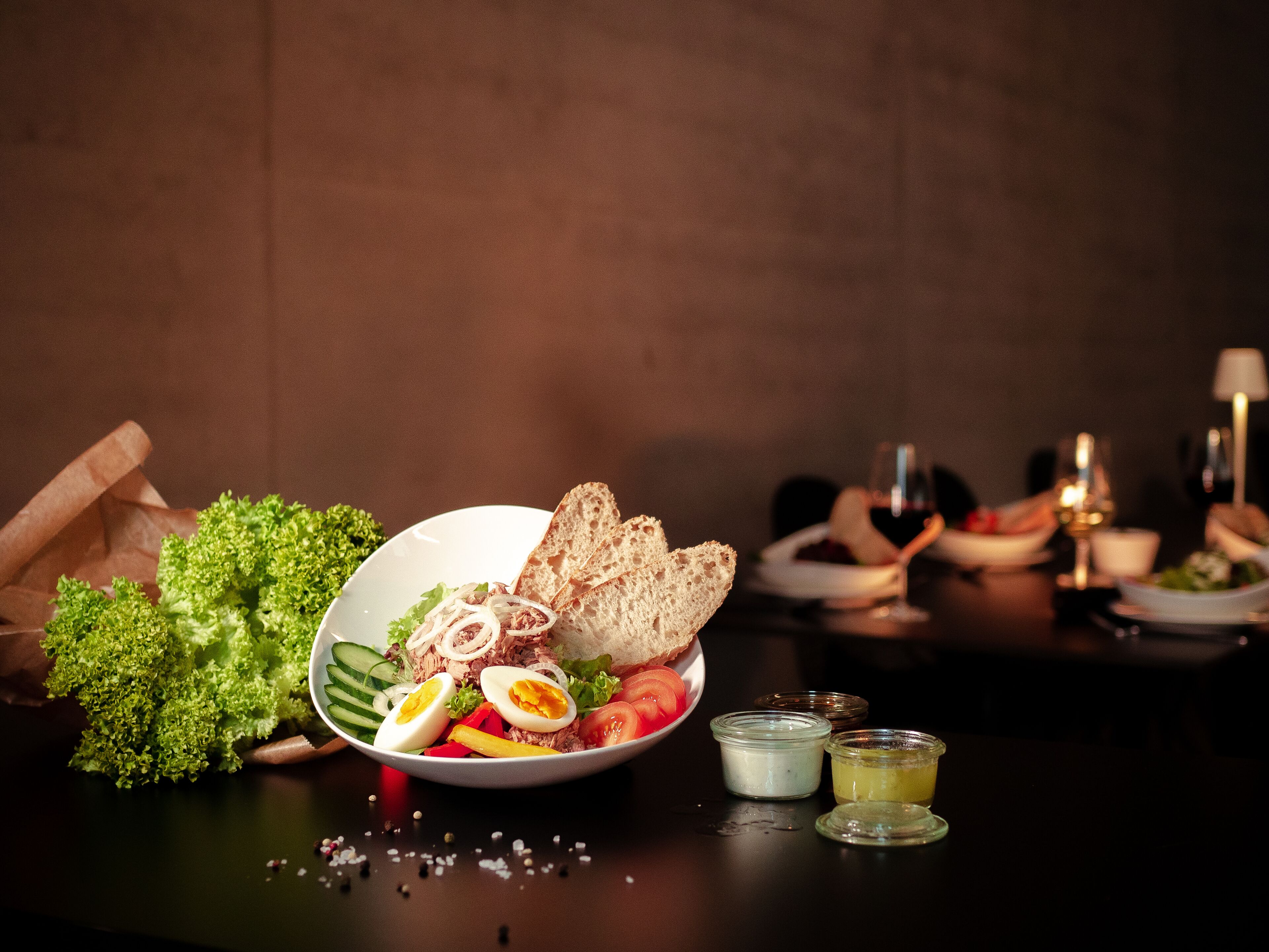 A dining table with a salad, bread, and condiments.