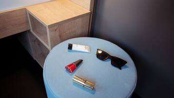 Ein kleiner, runder Hocker mit blauer Sitzkissenauflage, eine Sonnencremetube, eine rote Flasche und eine Sonnenbrille darauf.