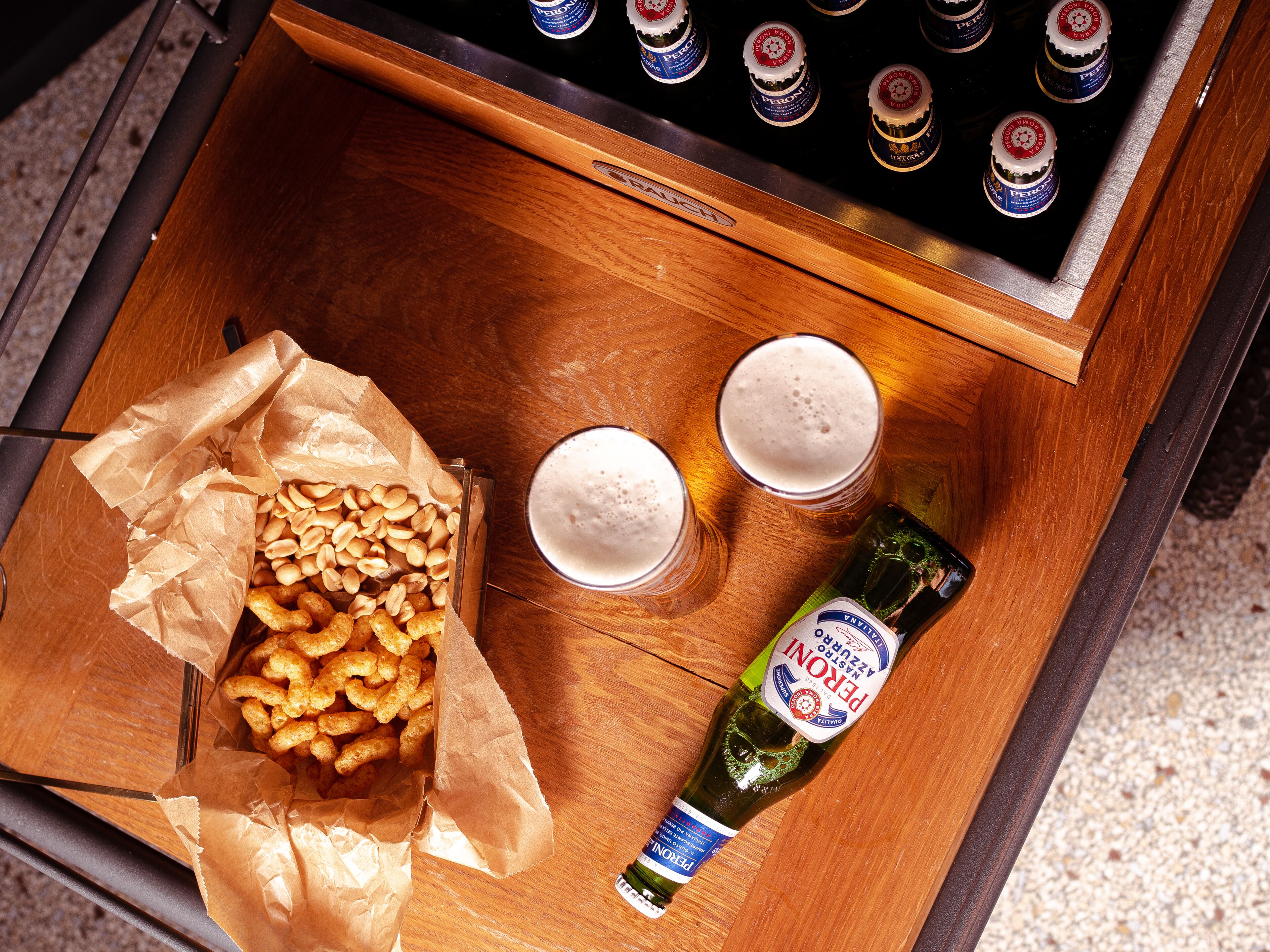 A tray with two glasses of beer, a bottle of beer, and a bag of snacks.