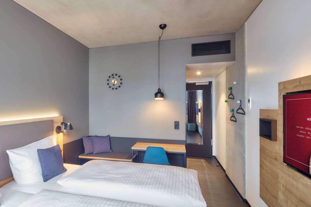 Una habitación de hotel moderna con cama, mesita de noche y un área de estar con mesa y sillas.