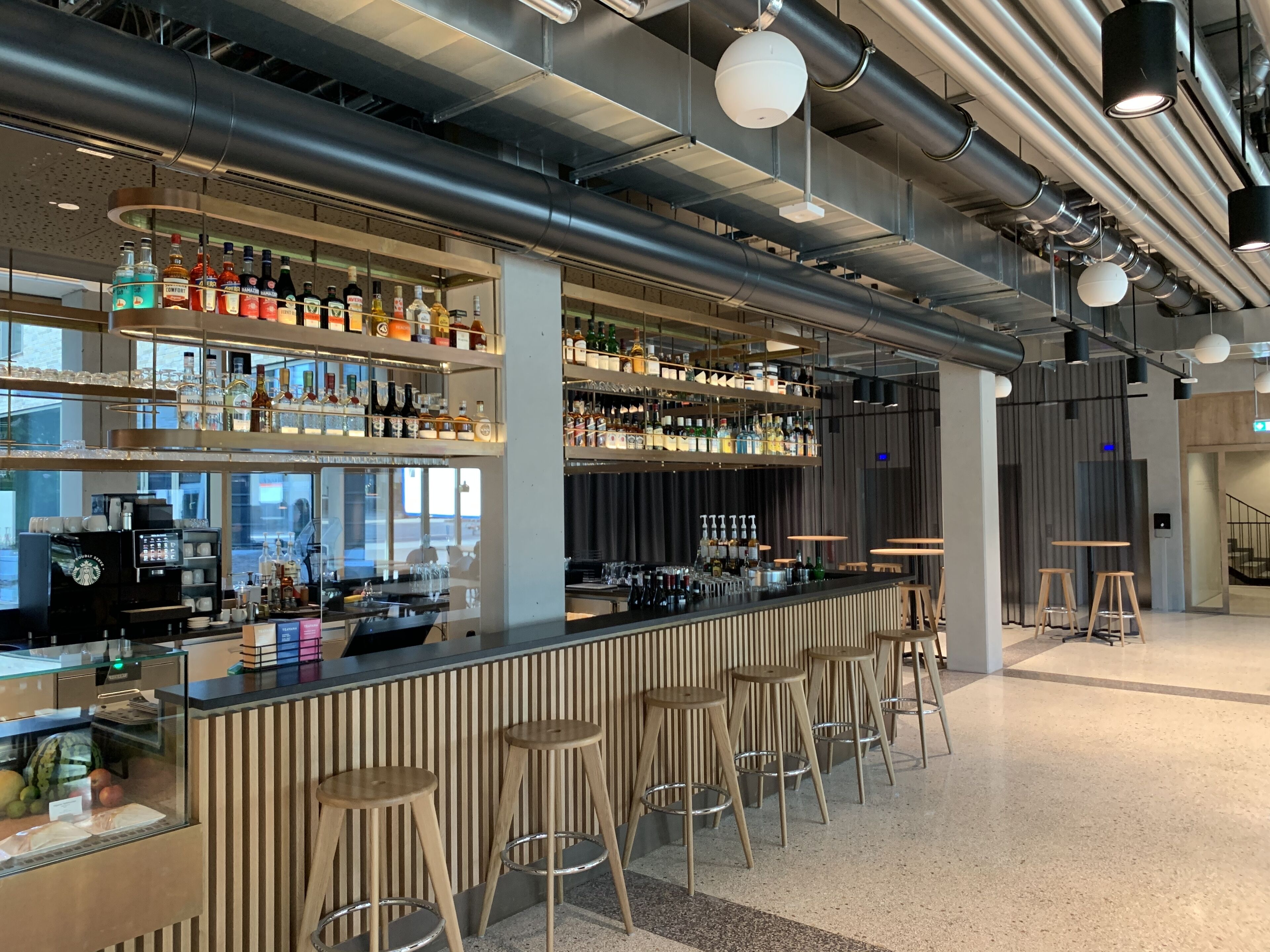 A modern bar with multiple liquor bottles, a coffee machine, and wooden stools.