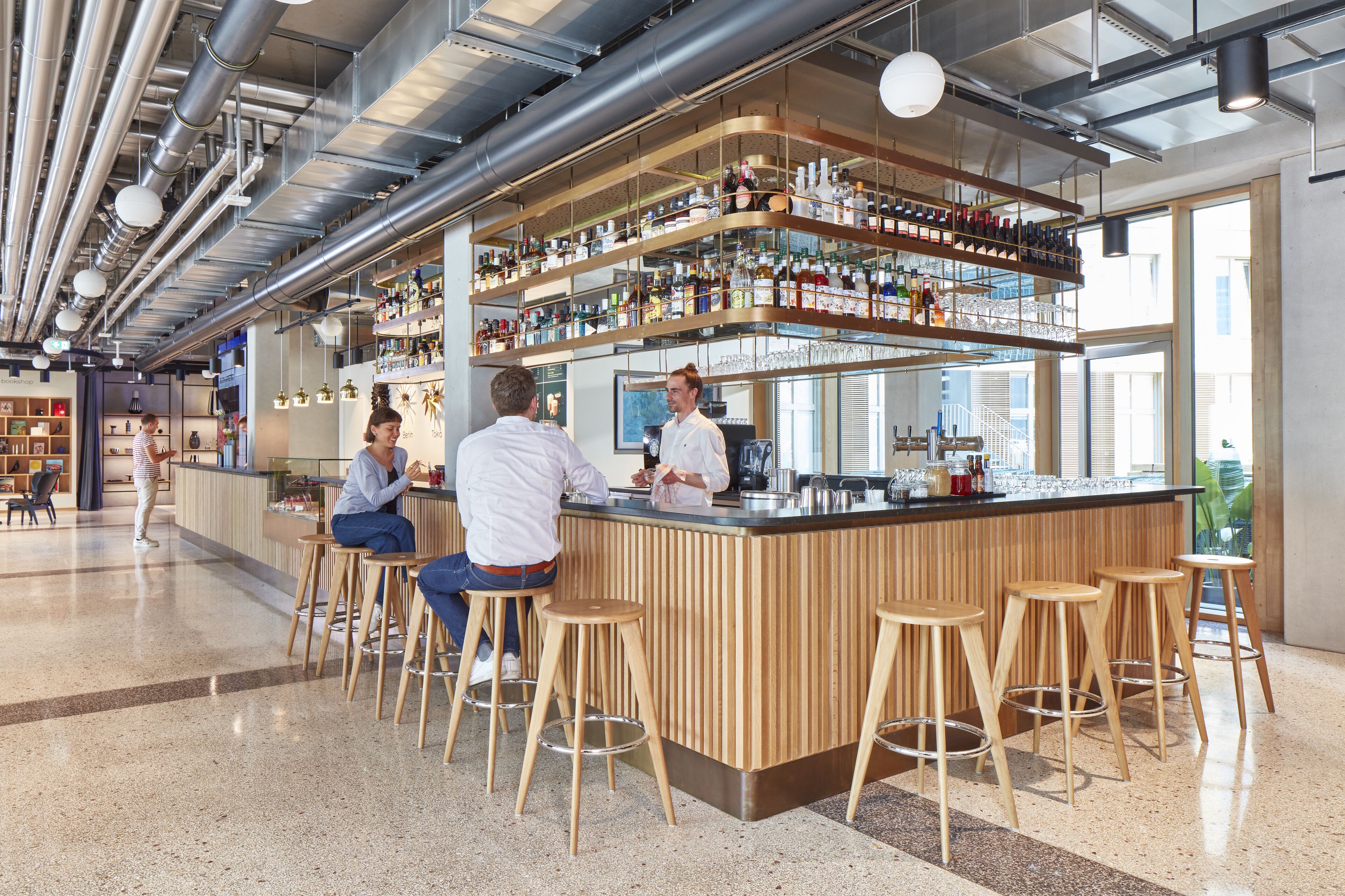 Ein moderner Barbereich mit Holzhockern, einer Bar und Regalen voller Flaschen und Gläsern.