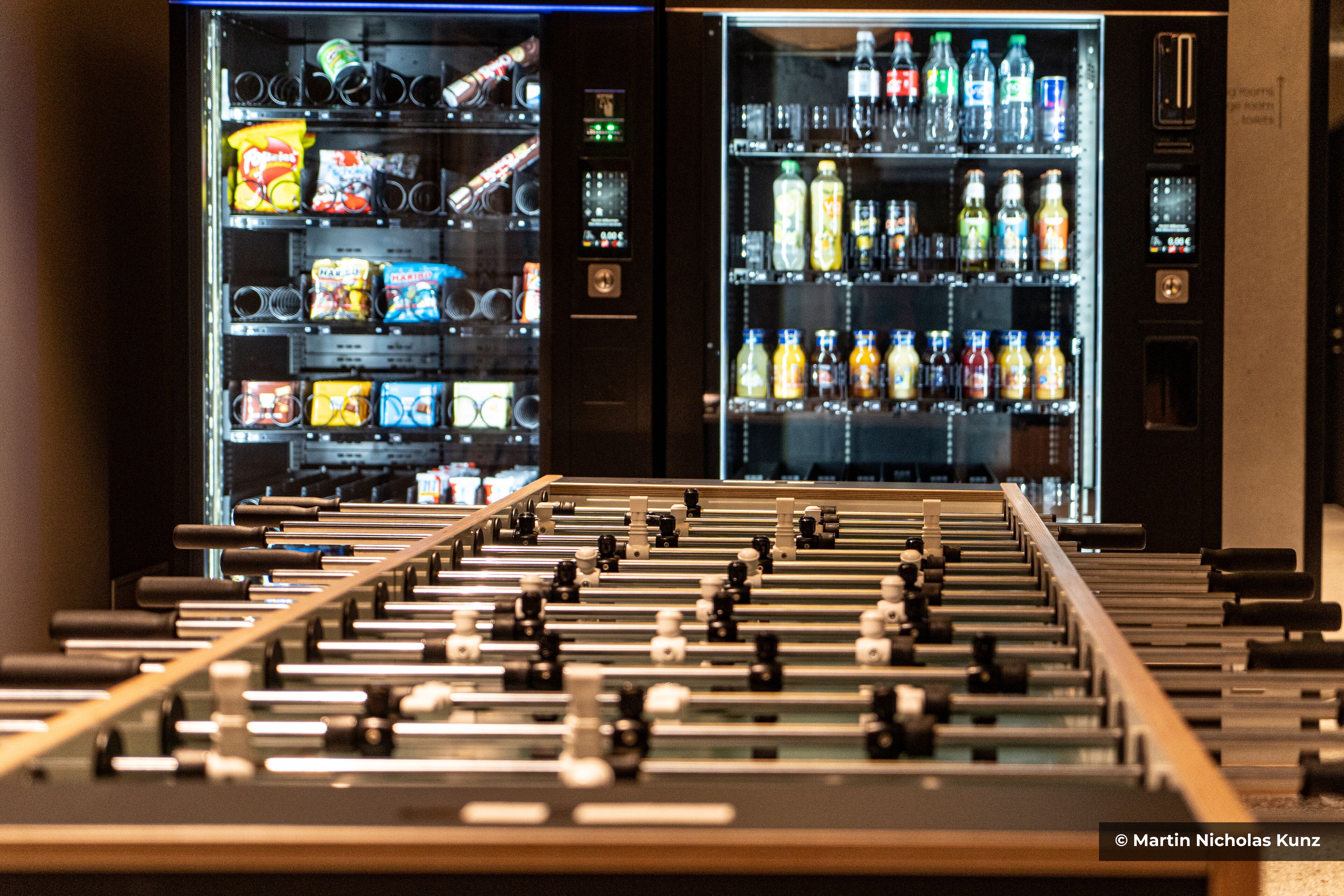 A foosball table in a bar area with two beverage vending machines in the background.