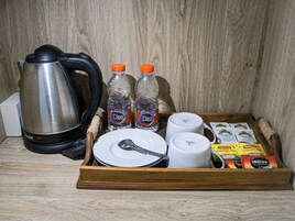 Uma bandeja de madeira com uma chaleira, duas garrafas de água, um prato com uma colher, duas chávenas brancas e vários saquinhos de chá e café.