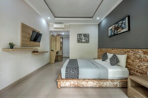 Un dormitorio moderno con cama, televisor montado en un panel de madera, escritorio con silla y armario.