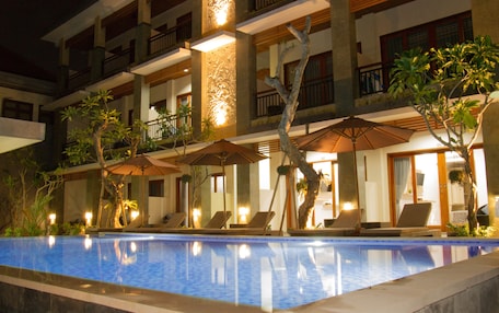 A hotel pool area with lounge chairs and umbrellas, surrounded by a multi-story building with balconies.