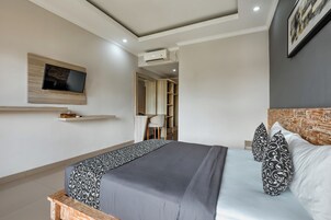 Quarto moderno com cama, televisão na parede, guarda-roupa e secretária.