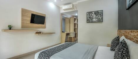 A modern bedroom with a bed, a mounted TV, a desk, and a wardrobe.