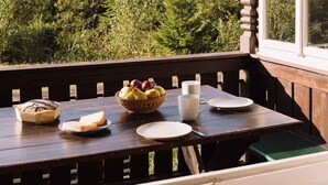 A wooden deck with a table set for breakfast, including bread, fruit, and a cup. - Berghütte Innsbruck (Innsbruck)