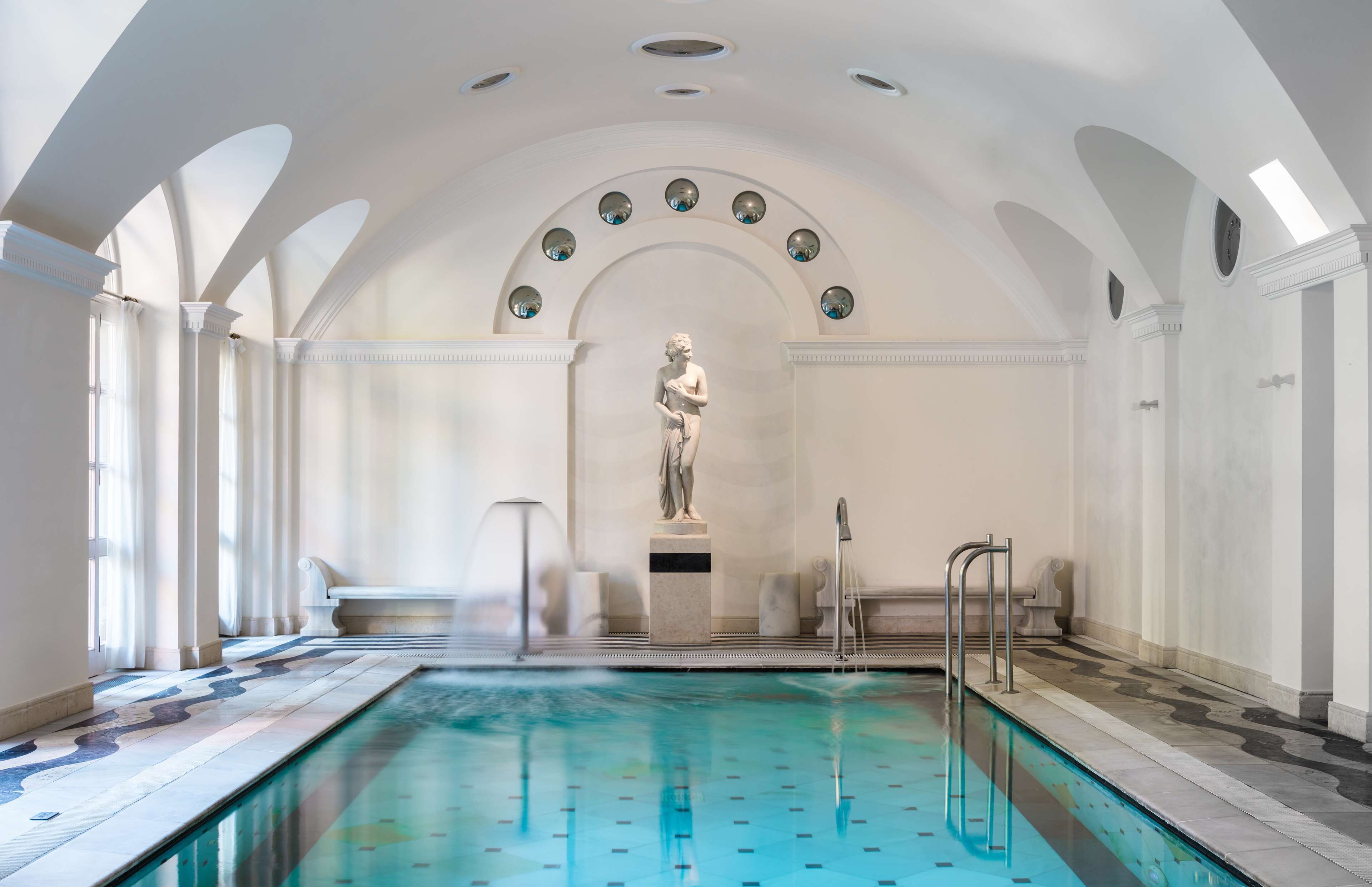 An indoor swimming pool with a statue in the center, surrounded by white columns and arches.