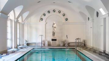 An indoor swimming pool with a statue in the center, surrounded by white columns and arches.