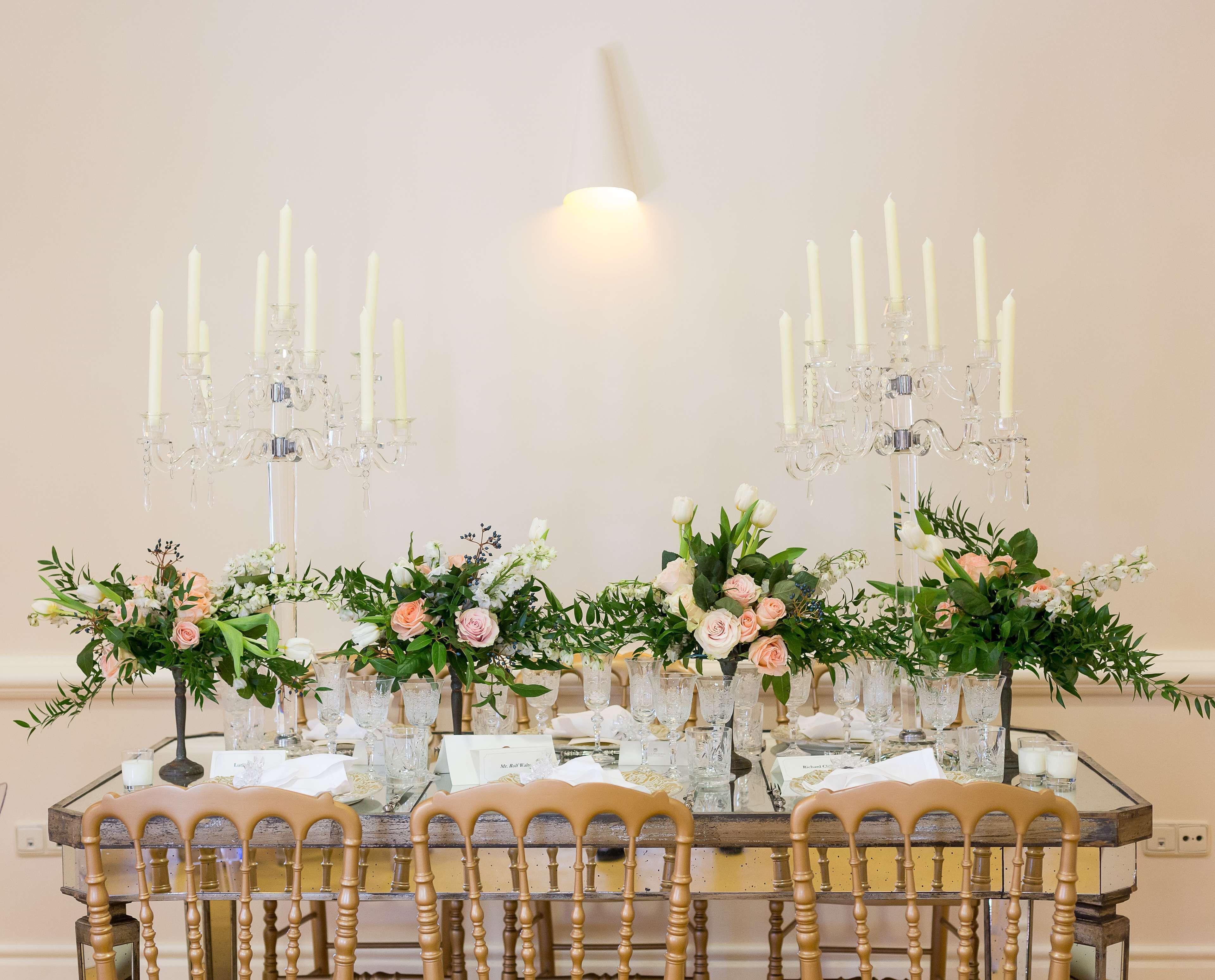 A table set for a formal event with multiple candle holders, floral centerpieces, and clear glassware.