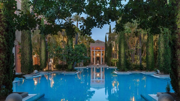 Una piscina rodeada de árboles altos y un edificio con columnas al fondo.