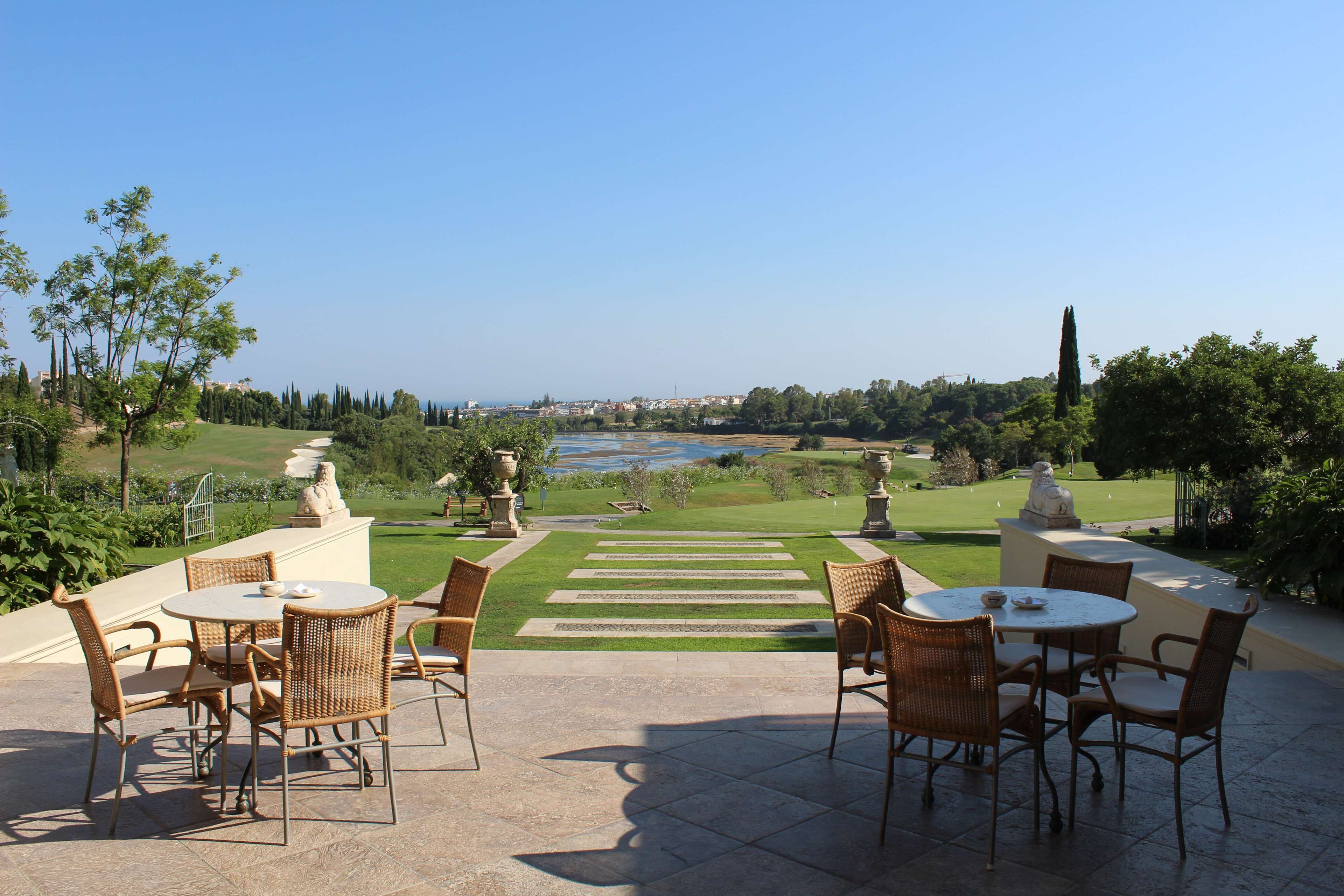 A patio with wicker furniture and a view of a golf course and water body.