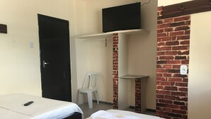 A room with two beds, a TV on a shelf, a brick wall, and a white chair. - Barra Mar Pousada e Restaurante (Salvador)