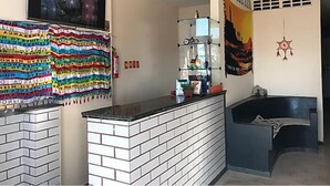 A reception area with a tiled counter, a television mounted on the wall, and a colorful fabric decoration. - Barra Mar Pousada e Restaurante (Salvador)