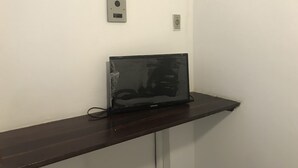 A laptop on a wooden desk against a white wall, with a power outlet and a light switch visible. - Barra Mar Pousada e Restaurante (Salvador)