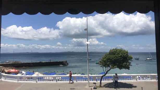 A coastal view with a paved walkway, umbrellas, and a tree. - Barra Mar Pousada e Restaurante (Salvador)
