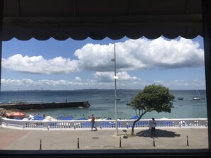Vista costera con un paseo adoquinado, sombrillas y un árbol.