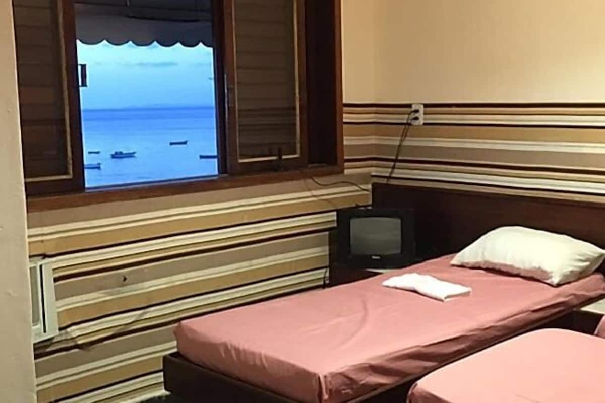 Una habitación con una cama, televisión y ventana con vista al mar.