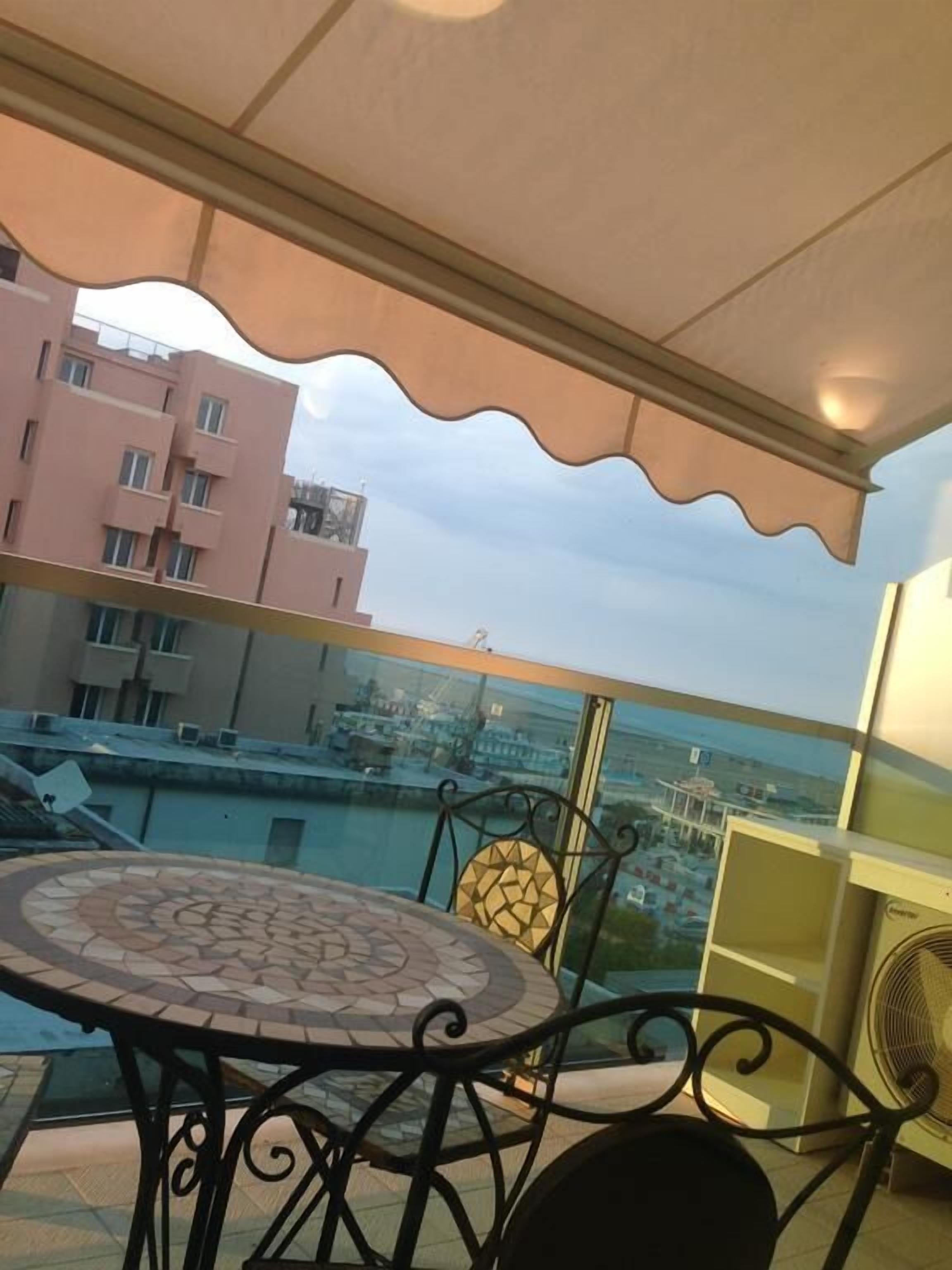 Un balcón con mesa y sillas, con vistas a un puerto deportivo y edificios.