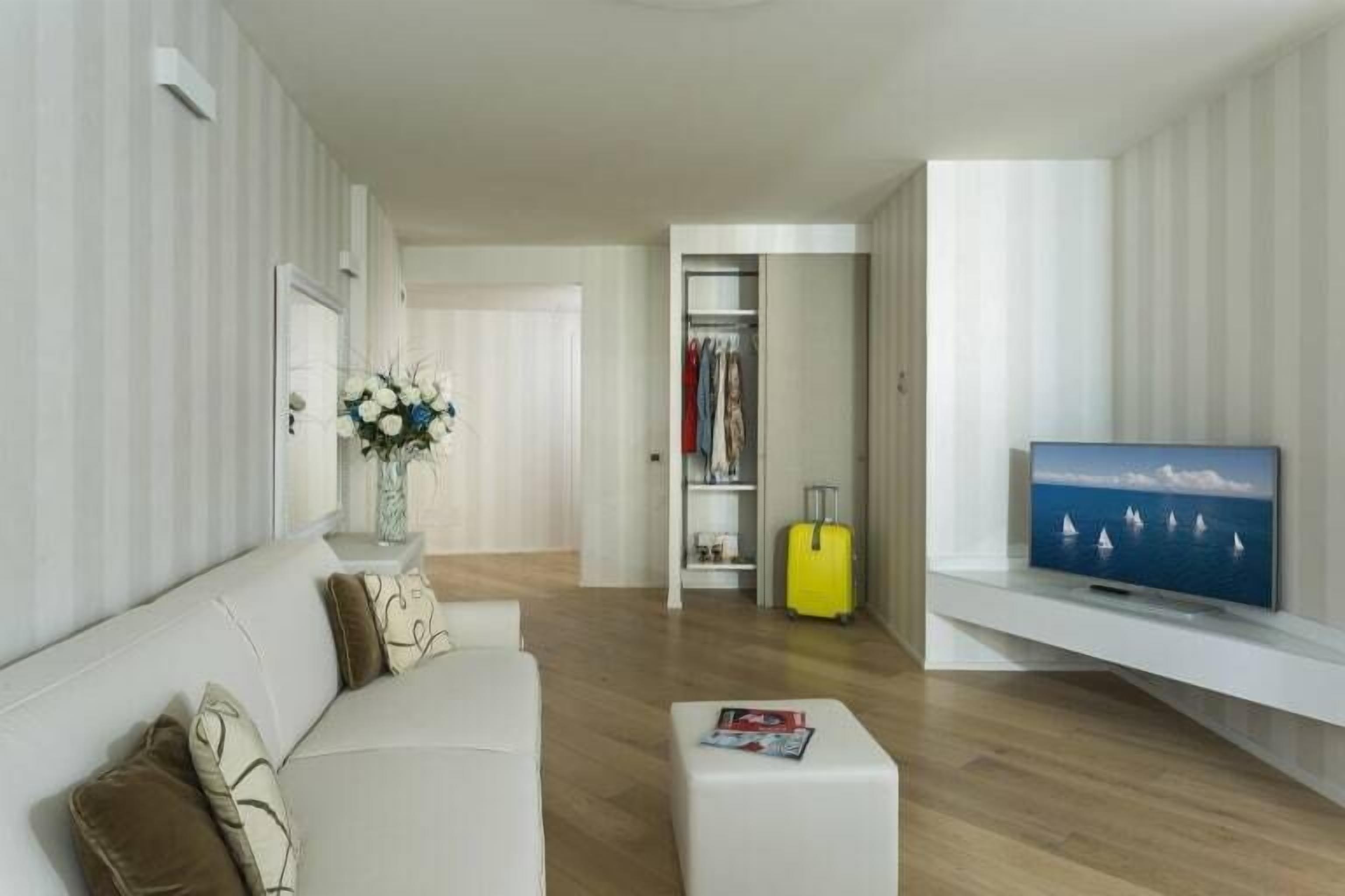 Un soggiorno moderno con un divano bianco, una televisione a schermo piatto e un pavimento in legno.