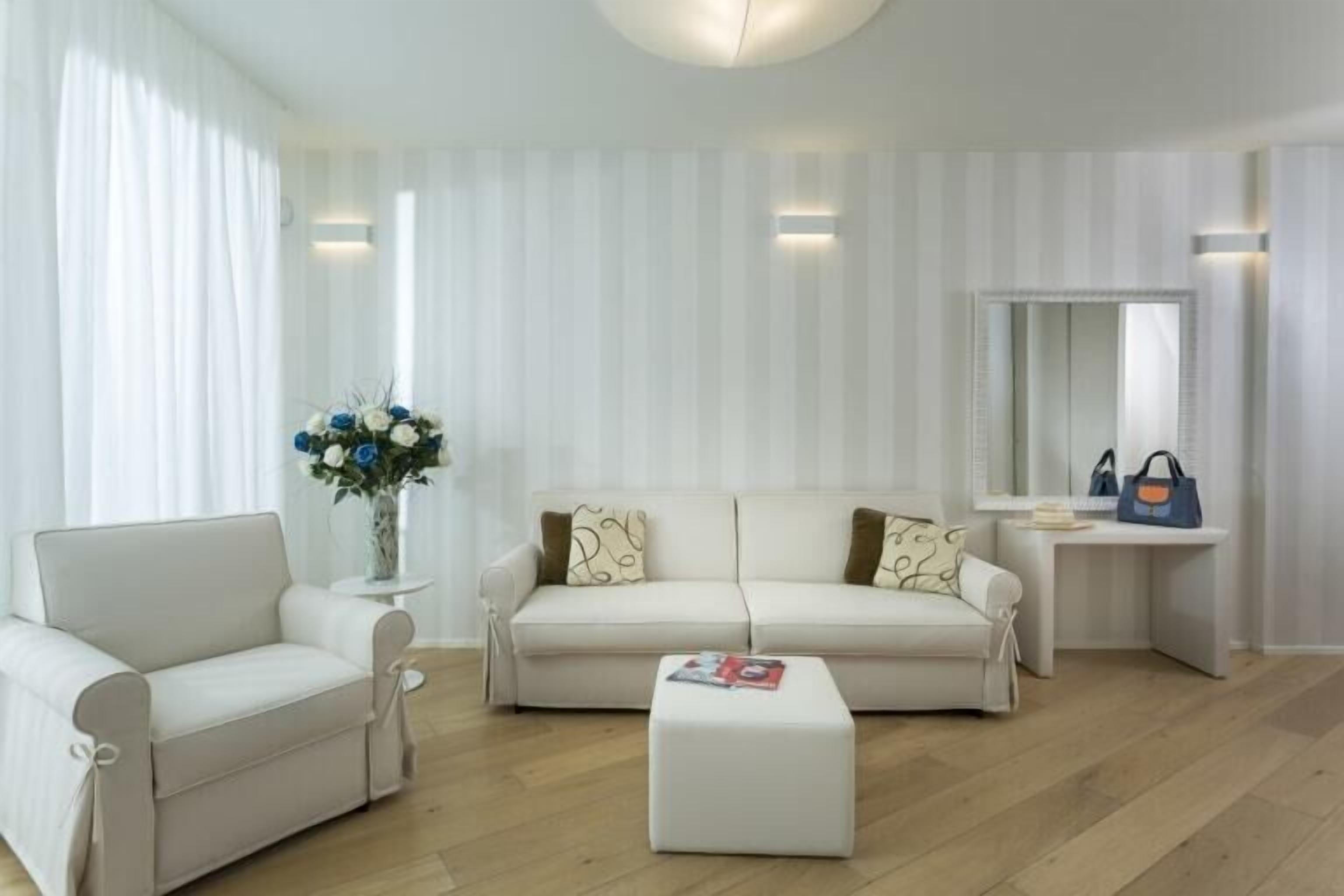 A modern living room with a sofa, ottoman, and a small table with a vase of flowers.