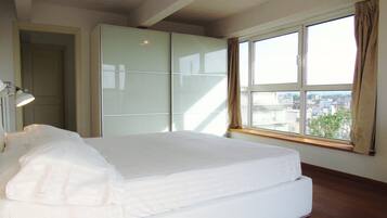 Een slaapkamer met een bed, een kledingkast, een bureau en een raam met uitzicht op gebouwen.