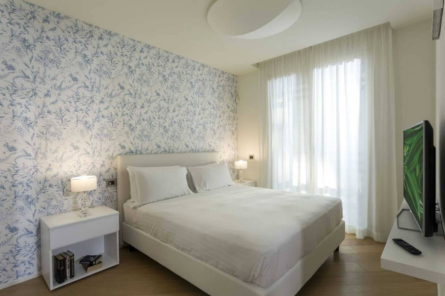 A bedroom with a large bed, two bedside tables with lamps, a TV, and a bookshelf.