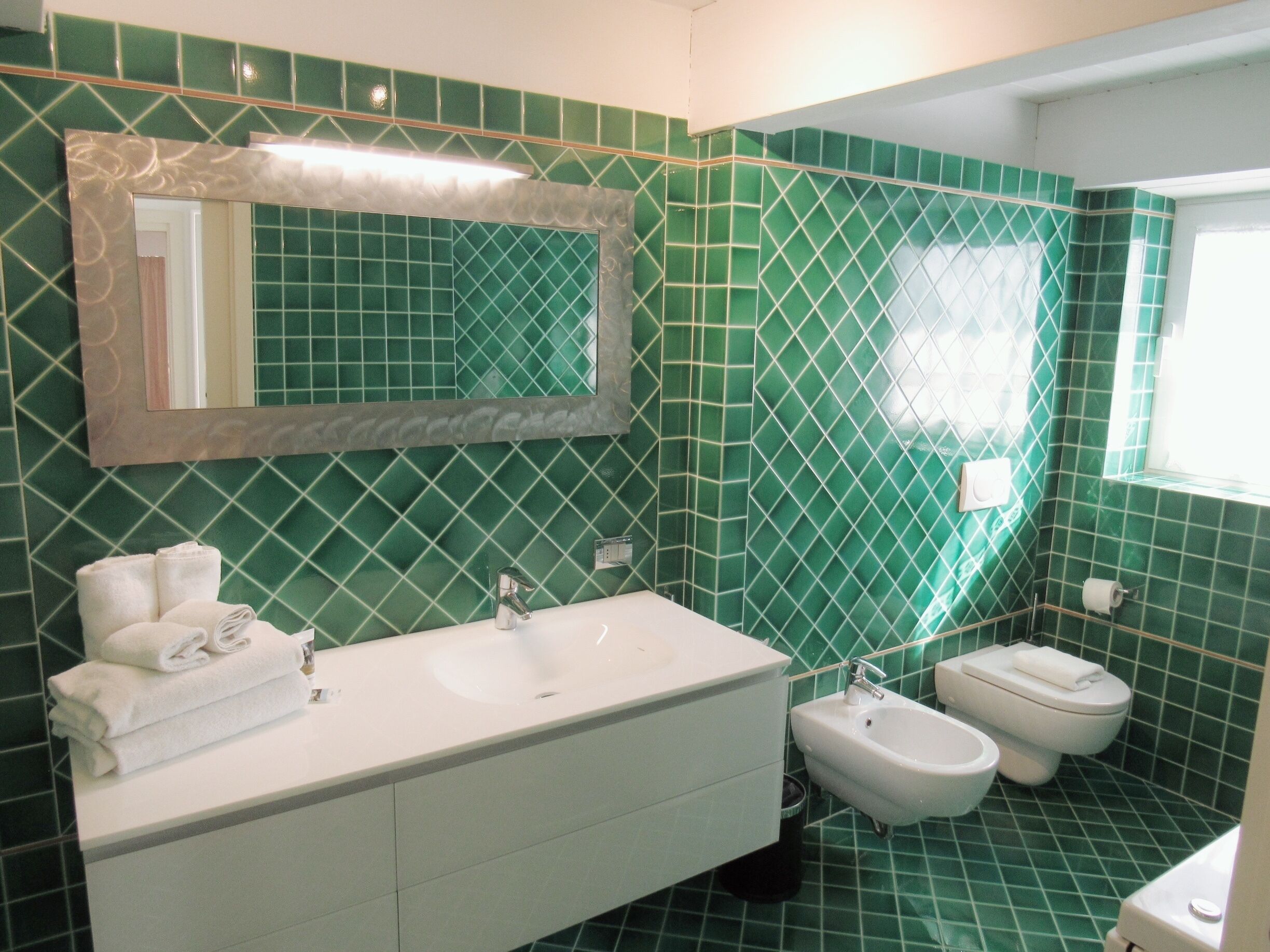 Een badkamer met groene betegelde wanden, een wit wastafel, een bidet en een toilet.