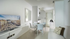 A modern living room with a flat-screen TV mounted on the wall, a dining area with a white table and chairs, and a sofa with a patterned cushion. - Embassy Aparthotel (Rimini)
