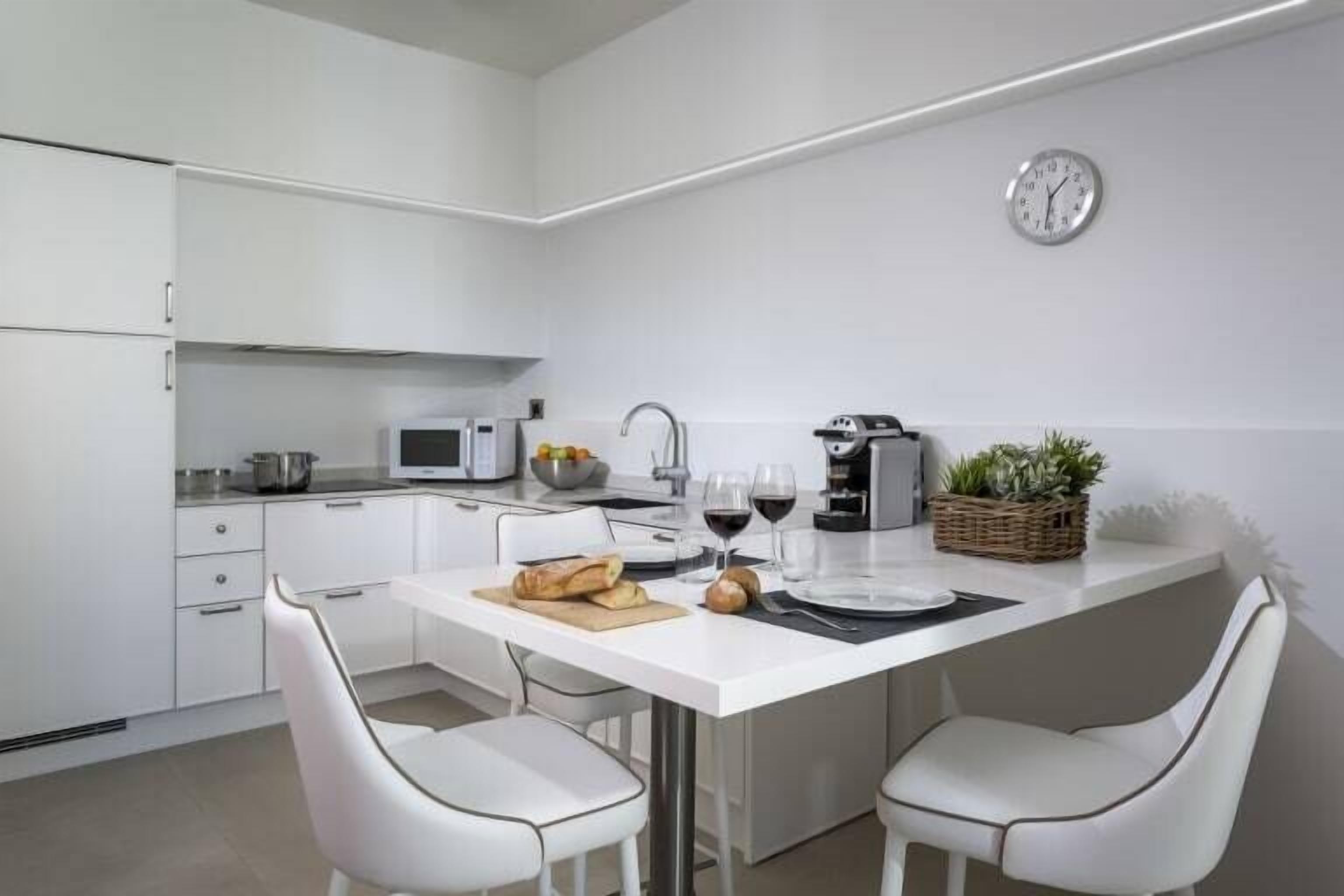 A modern kitchen with white cabinetry, a central island with seating, a microwave, and a clock on the wall.