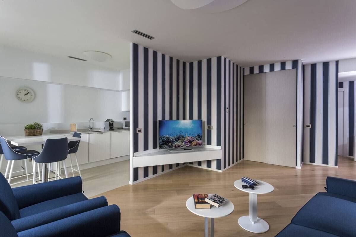 Una sala de estar moderna con televisor, papel tapiz a rayas y un comedor con sillas y mesa.