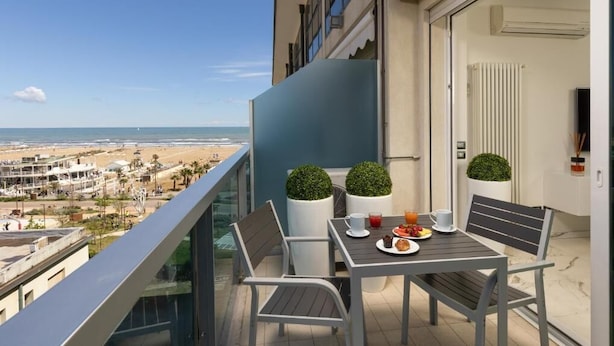 A balcony with a table set for breakfast, overlooking a beach and cityscape. - Embassy Aparthotel (Rimini)