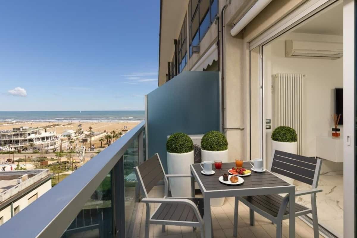 Un balcón con mesa lista para el desayuno, con vista a una playa y al paisaje urbano.