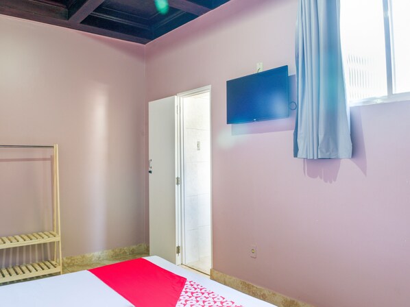 A room with a bed, a TV mounted on the wall, a door, and a window with curtains.