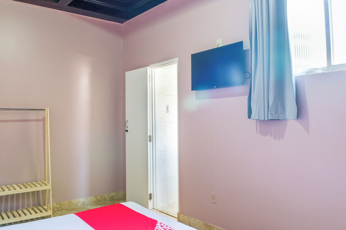 Een kamer met een bed, een aan de muur bevestigde televisie, een deur en een raam met gordijnen.