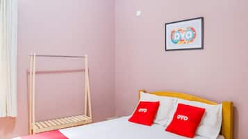A single bed with a wooden headboard, two red pillows with the word 'OYO' on them, a white blanket, and a wooden drying rack against a pink wall.