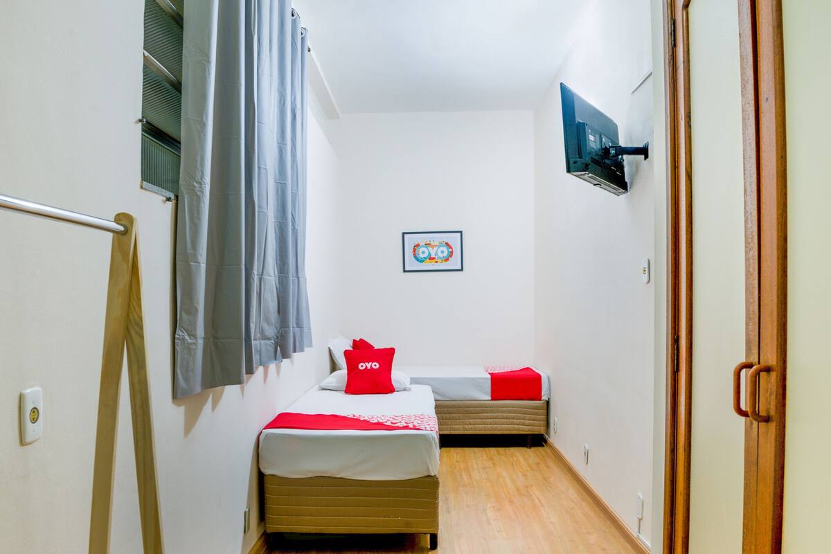 Ein kleiner, kompakter Raum mit Bett, einer kleineren Schlafmöglichkeit oder Couch, einem Fenster mit Vorhängen, einem wandmontierten Fernseher und einem gerahmten Bild.