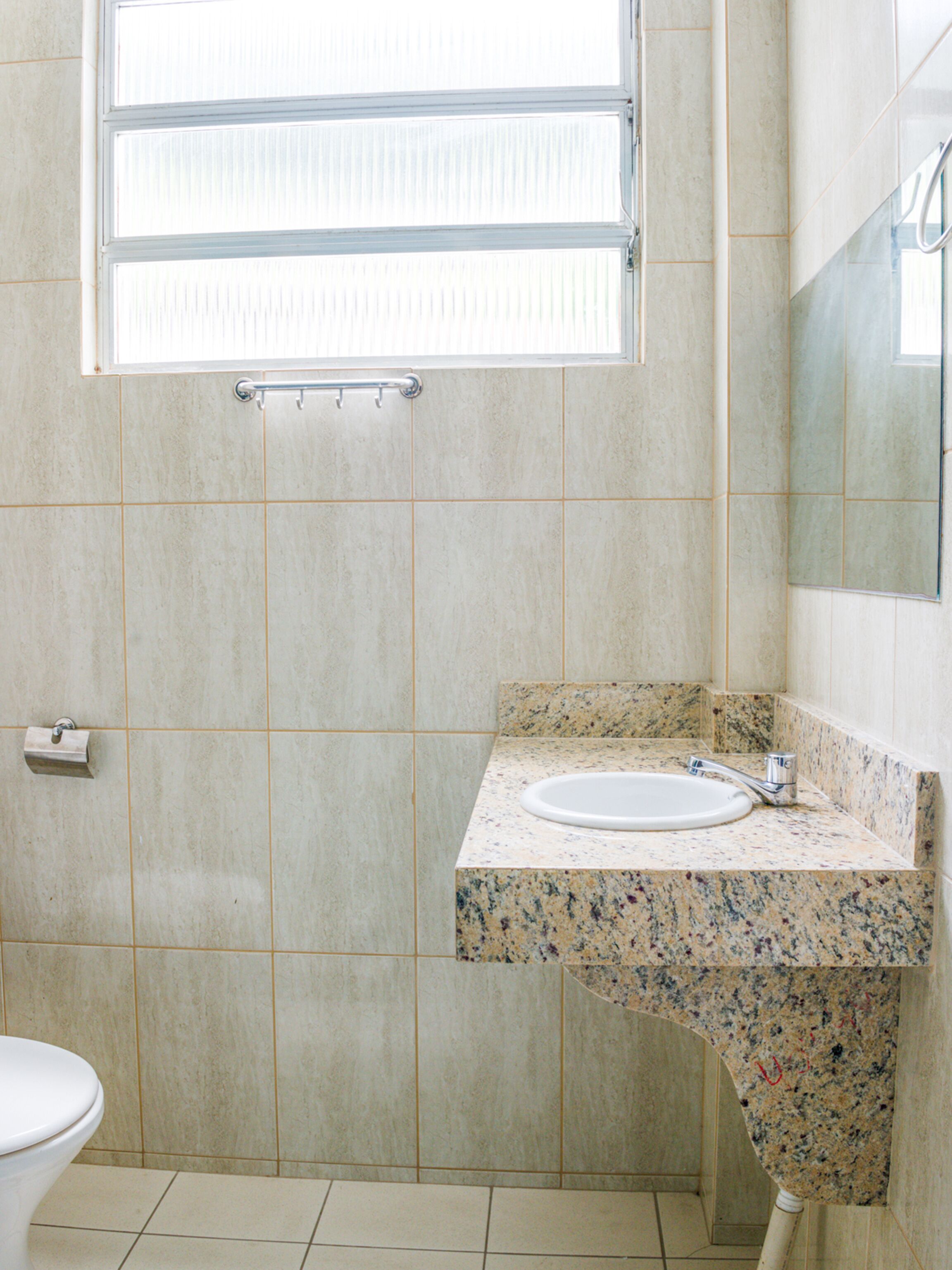 Un baño con inodoro, lavamanos con encimera de granito y ventana sobre el lavamanos.
