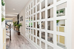 Un pasillo con suelo de madera, paredes blancas y una escalera con barandilla.