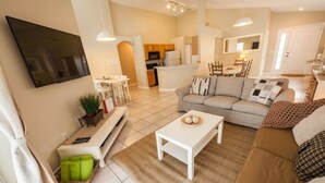 A modern living room with a sofa, coffee table, and TV. There is a kitchen area in the background.