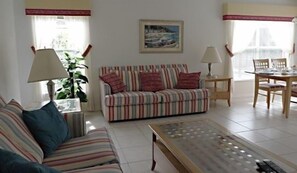 A living room with a striped sofa, a coffee table, a dining table with chairs, and a painting on the wall. - Great Pool Golf View 3 Bedroom Home by RedAwning (Haines City)