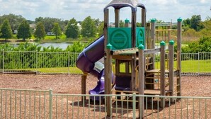 Een speeltuin met een glijbaan en klimconstructies, omringd door een hek en een waterpartij op de achtergrond.