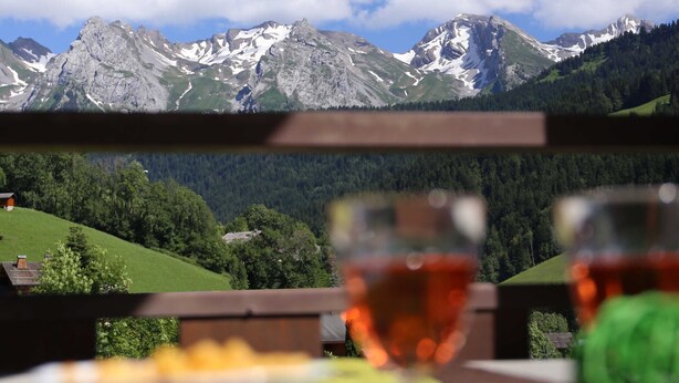 Une table avec un verre de vin rouge et une assiette de nourriture, le tout placé devant un paysage montagneux.